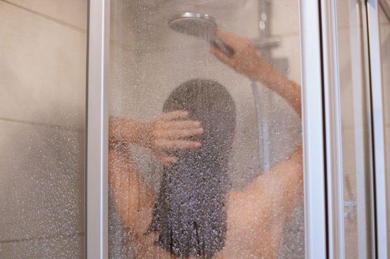 foto de um box de vidro com uma mulher de costas lavando o cabelo